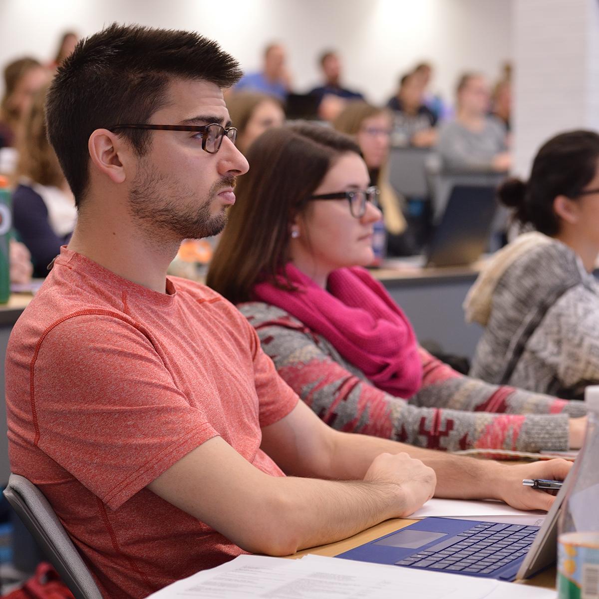 Photo of multiple students seated in a lecture hall, paying attention to an offscreen instructor